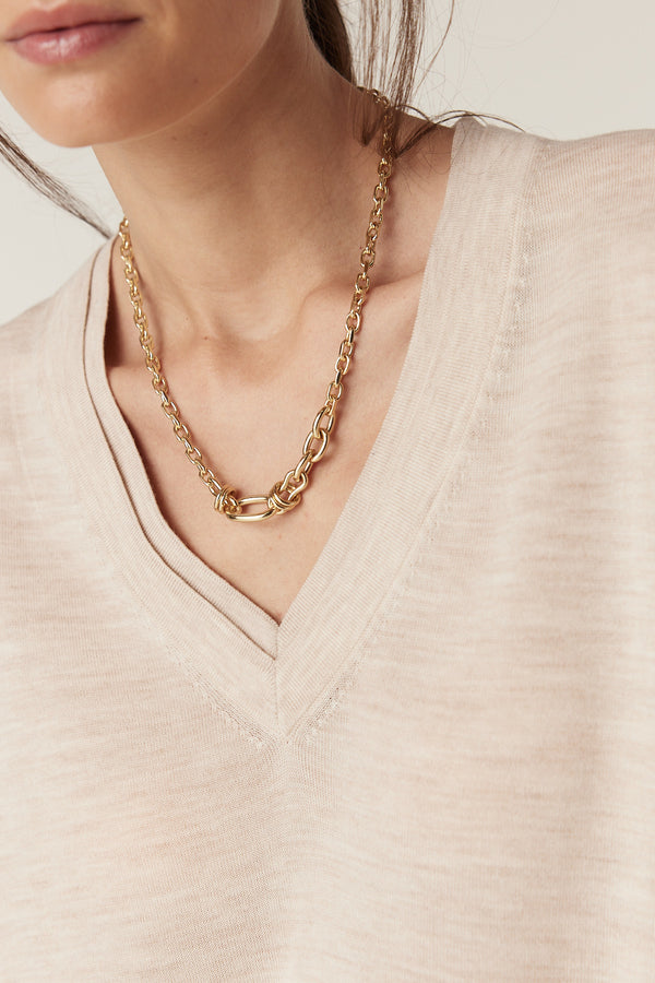 Close-up of an oatmeal fine merino wool V-neck jumper with a double collar trim and a gold chain necklace.