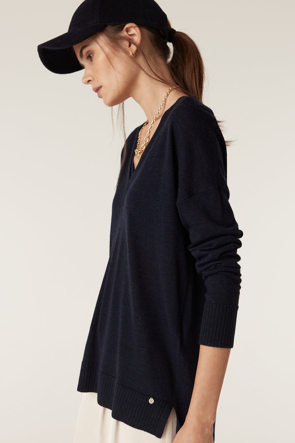 Woman in a Midnight Navy Merino wool V-neck jumper with dropped shoulders, rib cuffs, and a side split hem.