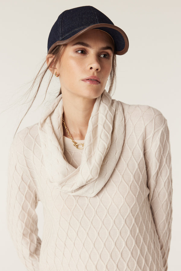 Woman wearing an antique white merino wool snood with diamond cable stitching and a cowl neck.