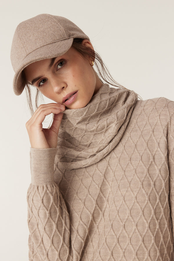 Woman wearing a pebble merino wool snood with diamond cable stitching and a matching baseball cap.