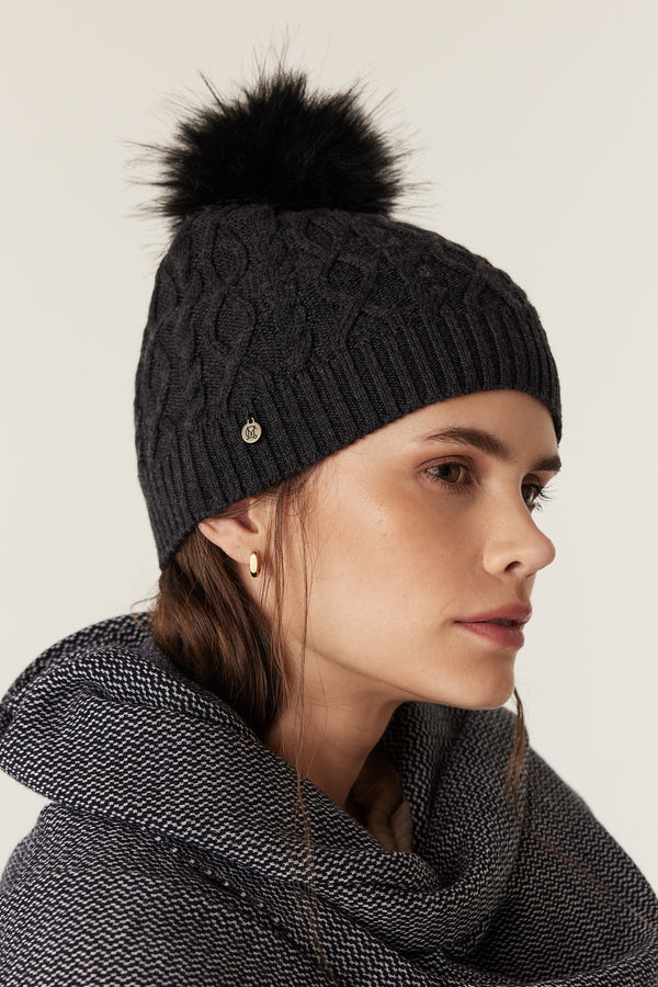 Charcoal merino wool beanie with diamond cable knit, ribbed hem, and detachable black faux fur pom pom.