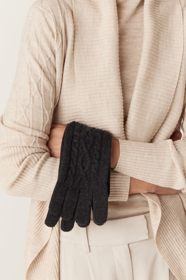 Charcoal merino wool gloves with diamond cable stitch, held by a person in a cream cardigan.