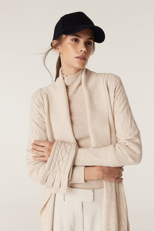 Woman wearing oatmeal Merino wool gloves with diamond cable stitch, mid-arm length, and ribbed hem.