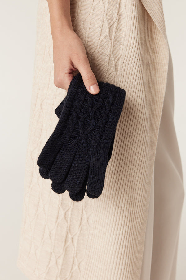 Midnight navy merino wool gloves with diamond cable knit held against a cream cable knit garment.
