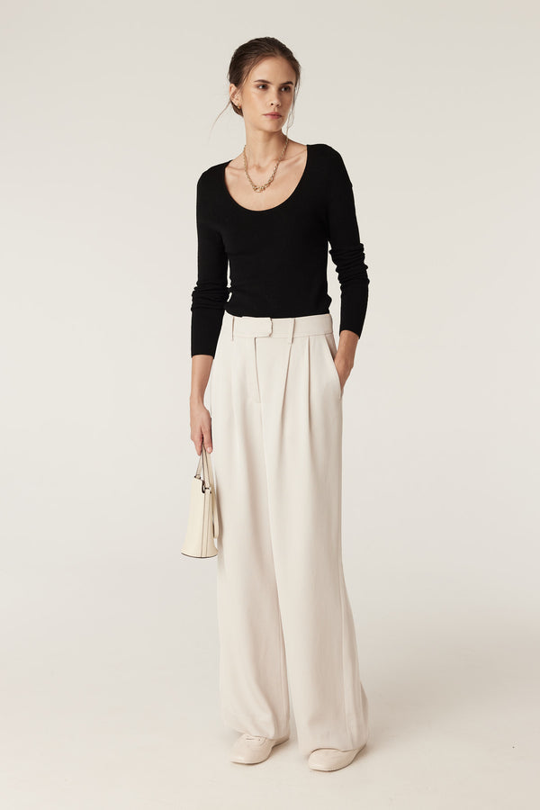 Model wears a black superfine merino scoop neck top with cream wide-leg pants and a small white handbag.