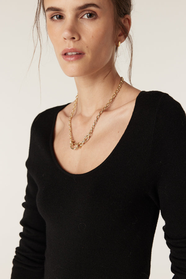 Woman wearing a black superfine merino wool scoop neck top with a gold chain necklace.