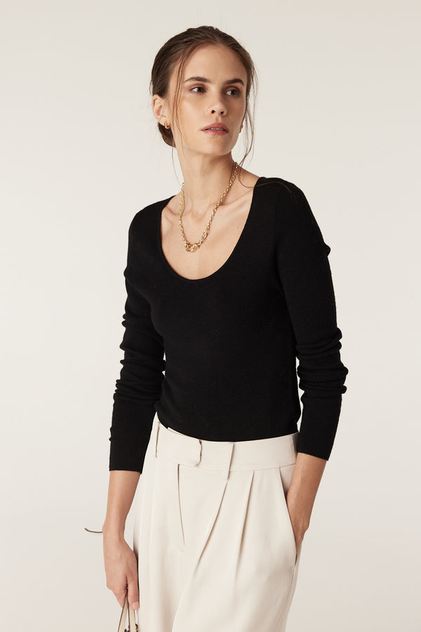 Woman wearing a black superfine merino wool scoop neck top with cream trousers.