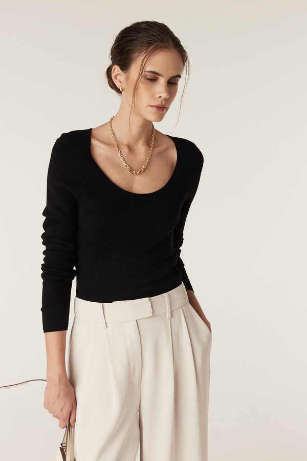 Woman wearing a black superfine merino scoop neck top with long sleeves, paired with cream trousers.