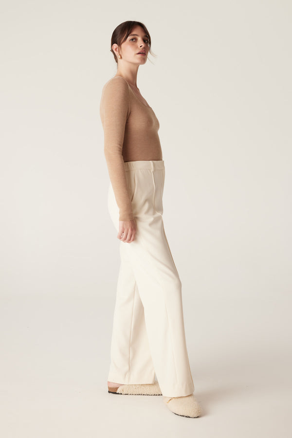 Woman wearing a camel superfine merino wool scoop neck top and cream wide-leg pants.