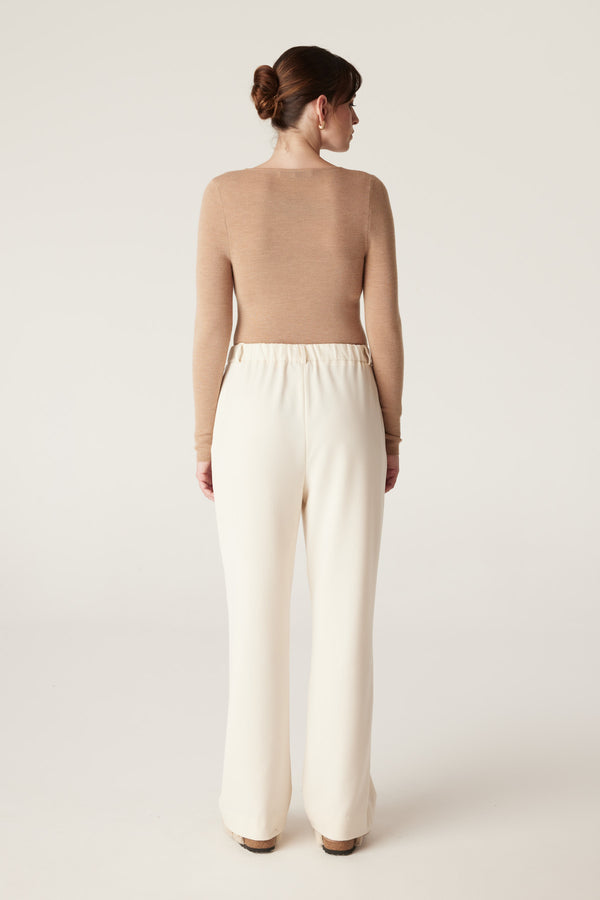 Woman from behind wearing a camel superfine merino scoop top and cream wide-leg pants.