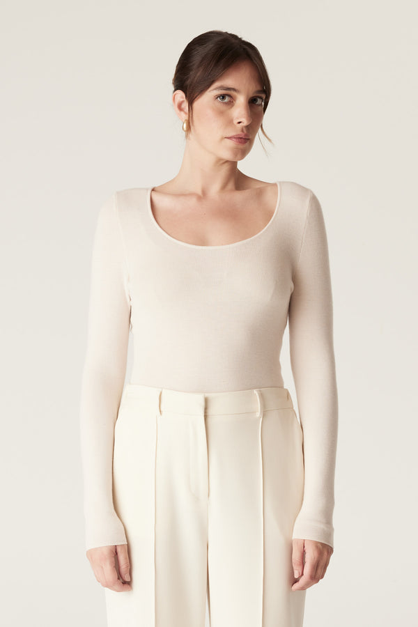 Woman wearing an ecru superfine merino wool scoop-neck top with long sleeves and cream trousers.