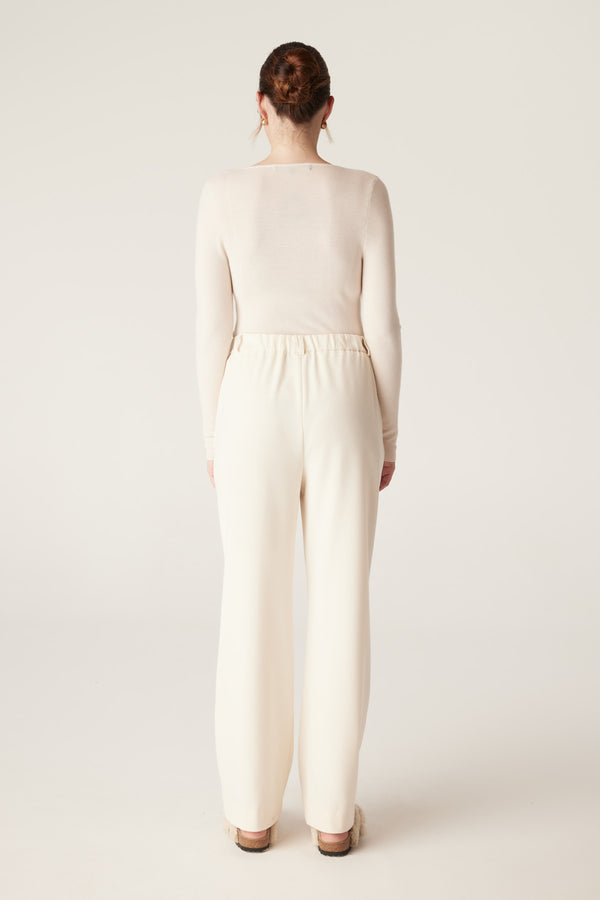 Model from behind wearing an ecru superfine merino wool scoop neck top and matching wide-leg pants.