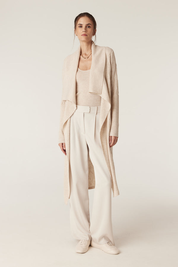 Woman wearing an oatmeal superfine merino scoop top, cream wide-leg pants, and a long cream cable-knit cardigan.