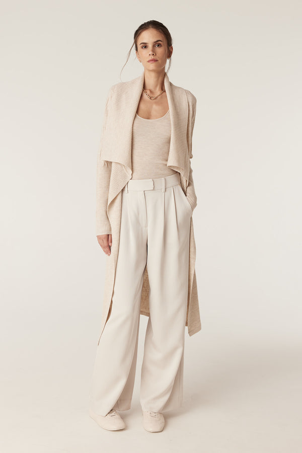Woman in oatmeal merino scoop top, long ribbed cardigan, and cream wide-leg pants.