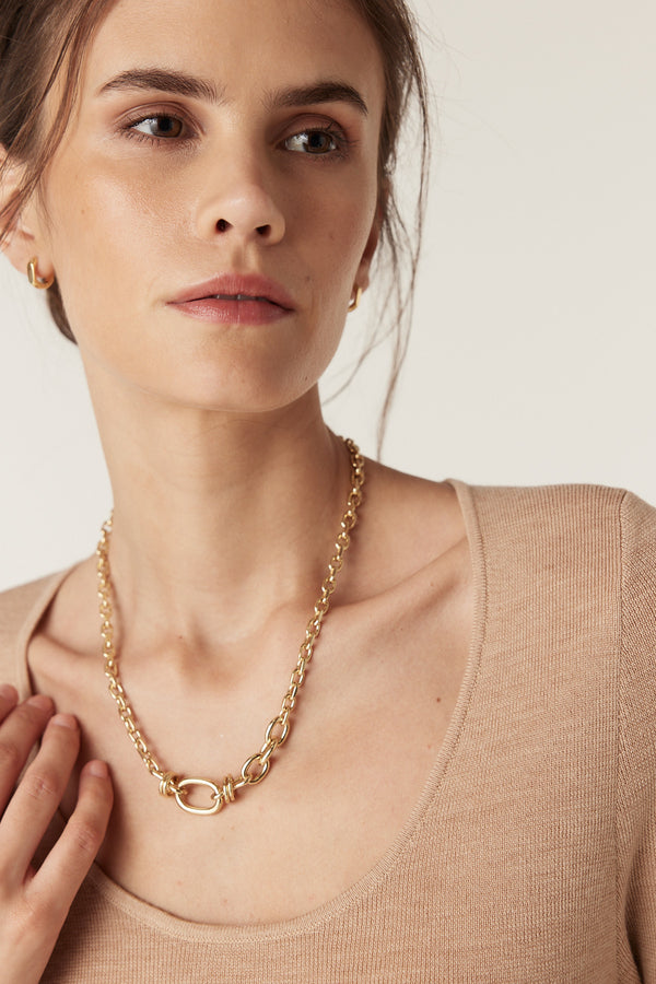 Woman in a slim-fit latte superfine merino wool scoop neck top, wearing a gold chain necklace.