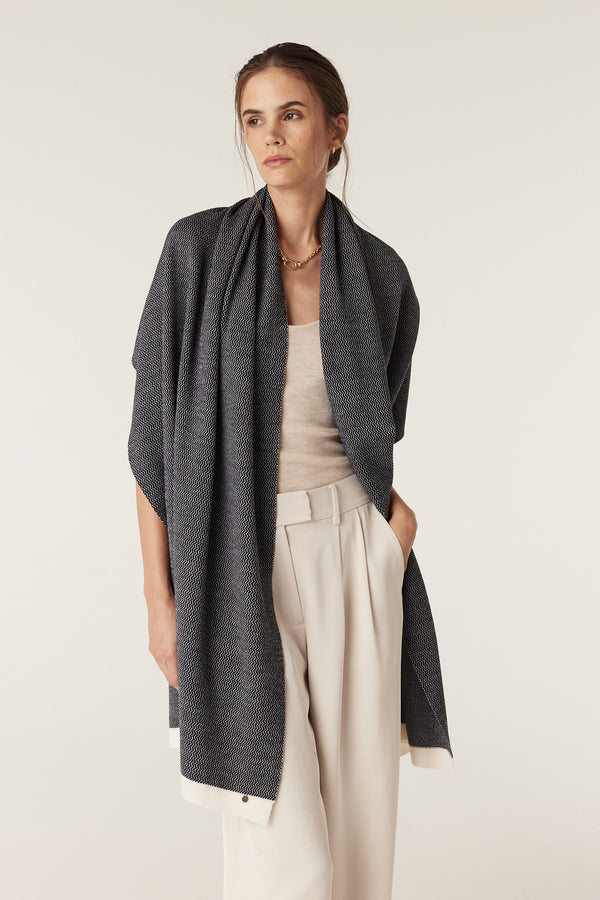 Woman wearing a Midnight Navy Merino wool wrap with a birdseye jacquard design, styled as a shawl.
