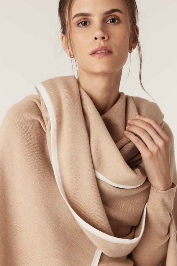 Woman wearing a latte merino wool cape with white contrast trim, draped elegantly around her shoulders.