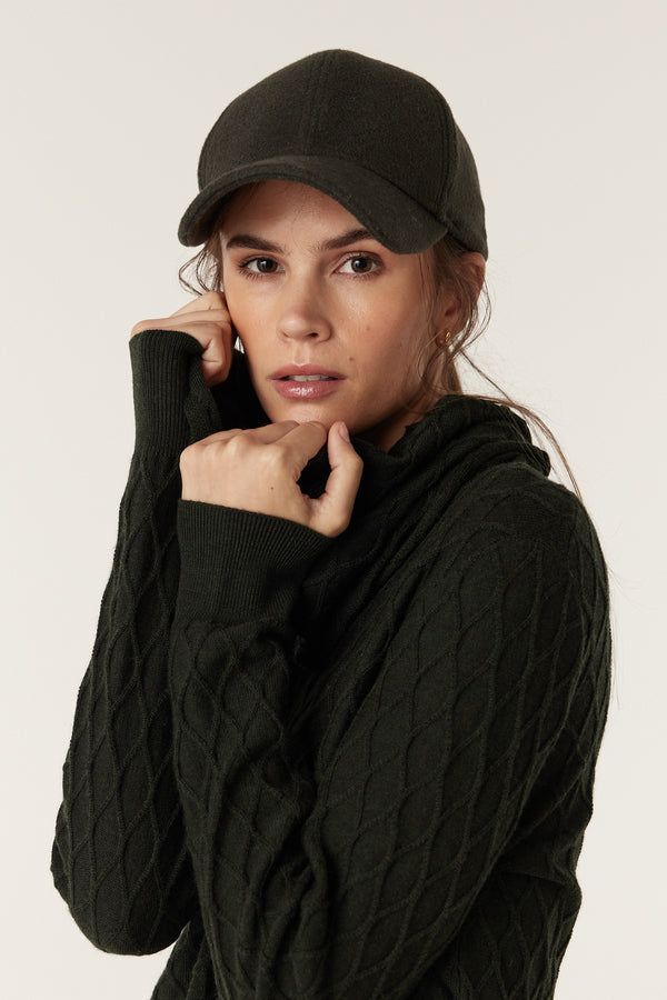 Woman wearing a moss green wool cashmere 6-panel cap with a 7cm peak and an adjustable back strap.