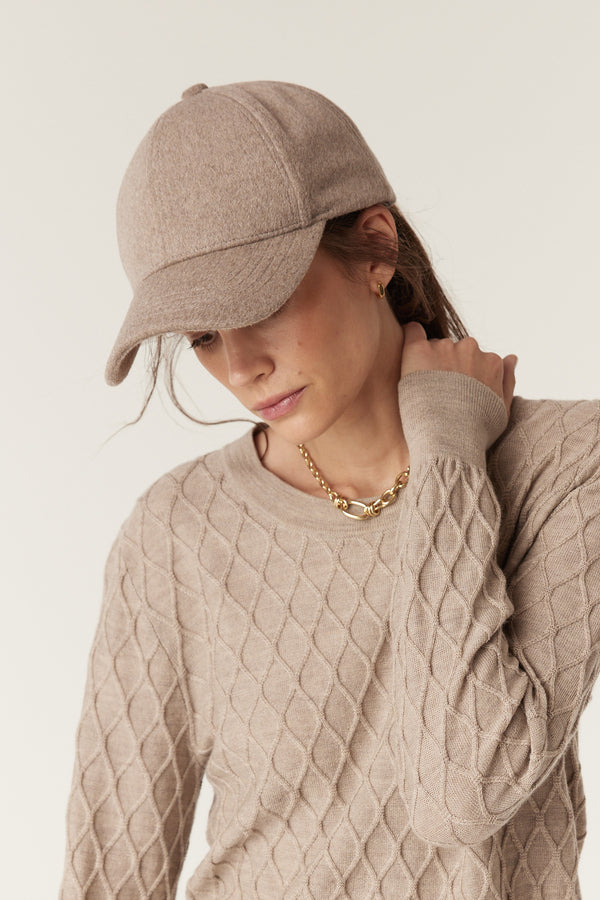 Pebble wool cashmere 6-panel cap with a curved peak on a model, paired with a textured beige sweater.