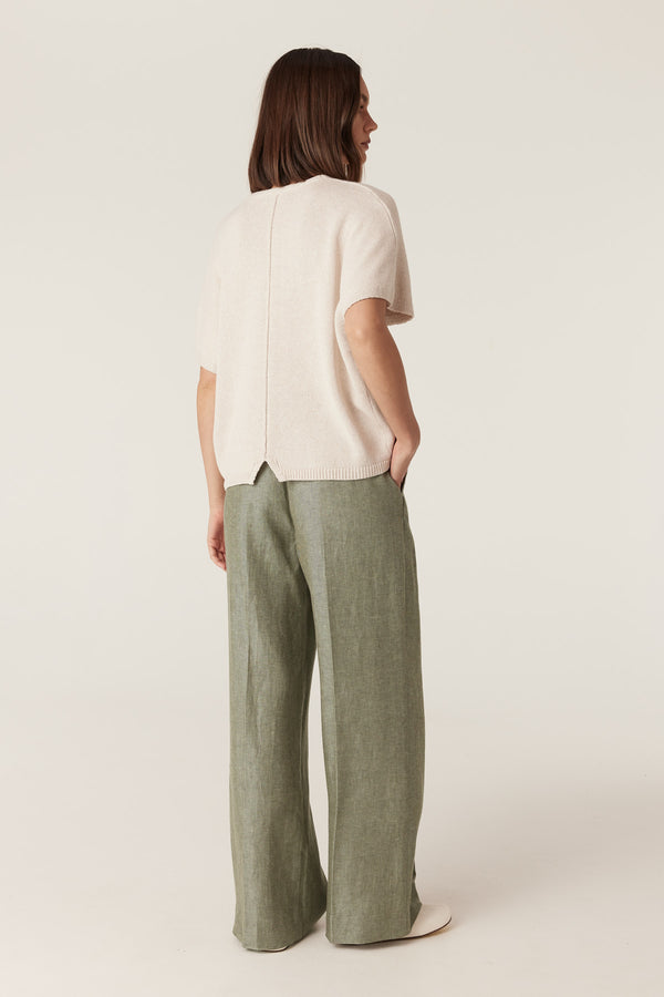 Model wearing a relaxed-fit, calico-colored knit top with a ribbed hem, paired with wide-leg olive green trousers.