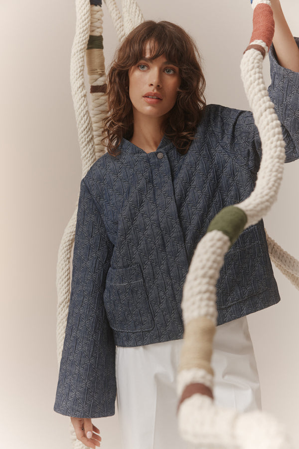 Model wearing a relaxed-fit, blue denim quilted jacket with a rope-inspired pattern, patch pockets, and flared sleeves.