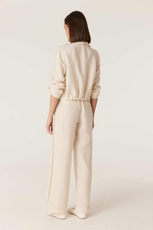 Back view of a woman wearing an ecru Goldie jacket with a toggle hem and matching wide-leg trousers.