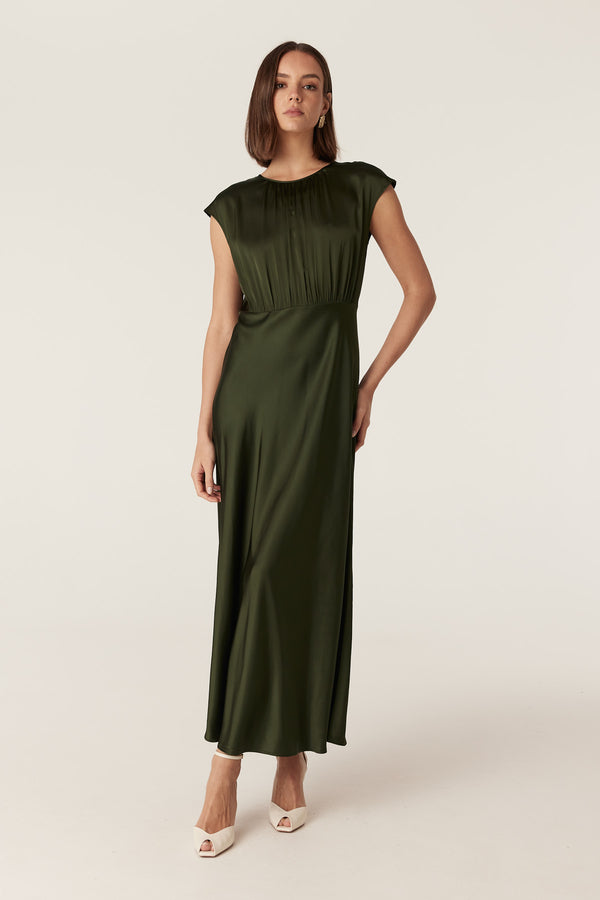 Dark green Muse dress in fluid stretch fabric with cap sleeves, gathered bodice, and a draped bias-cut skirt.