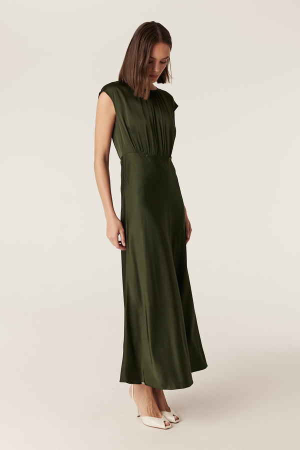 Dark green Muse dress in fluid stretch fabric with cap sleeves, a gathered bodice, and a draped bias-cut skirt.