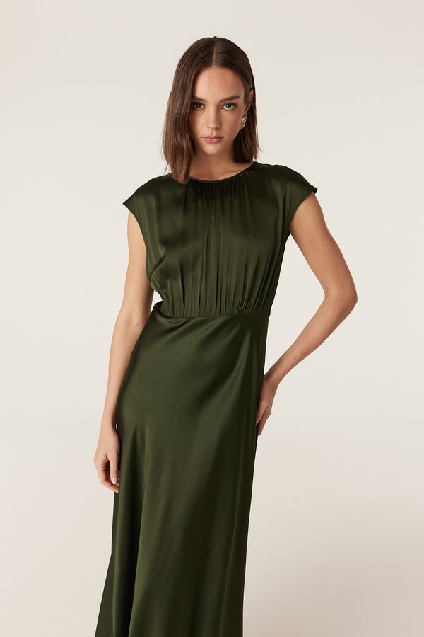Dark green Muse dress in fluid stretch fabric with cap sleeves, gathered bodice, and a draped bias-cut skirt.