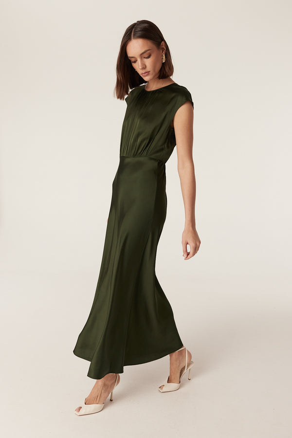 Dark green Muse dress in fluid stretch fabric with cap sleeves, gathered bodice, and a draped bias-cut skirt.