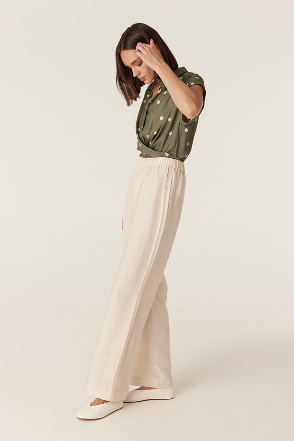 Green polka dot collared blouse with cap sleeves paired with cream wide-leg trousers on a model.