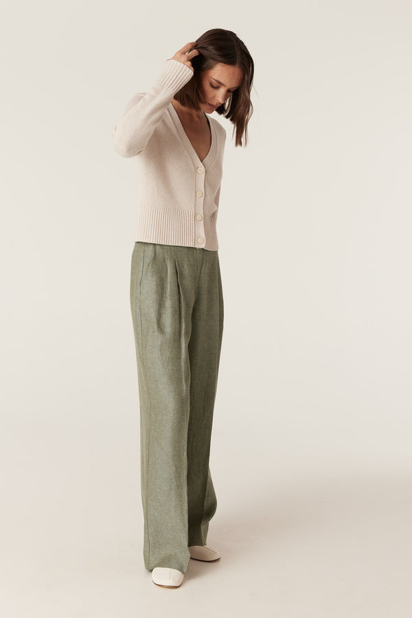 Model wearing green wide-leg French linen pants with front pleats, belt loops, and a beige button-down cardigan.