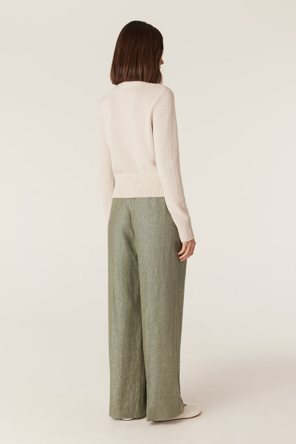Back view of green wide-leg Evelyn linen pants paired with a cream knit sweater on a neutral background.