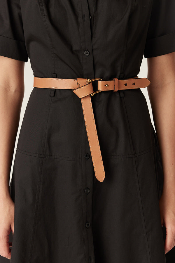 Tan leather belt with a polished gold-tone buckle, styled in a knot over a black button-down dress.
