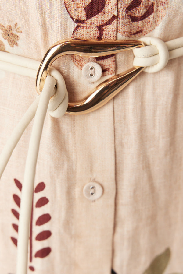 Ivory Venetian leather belt featuring a sculptural gold-tone buckle worn over a patterned linen dress.